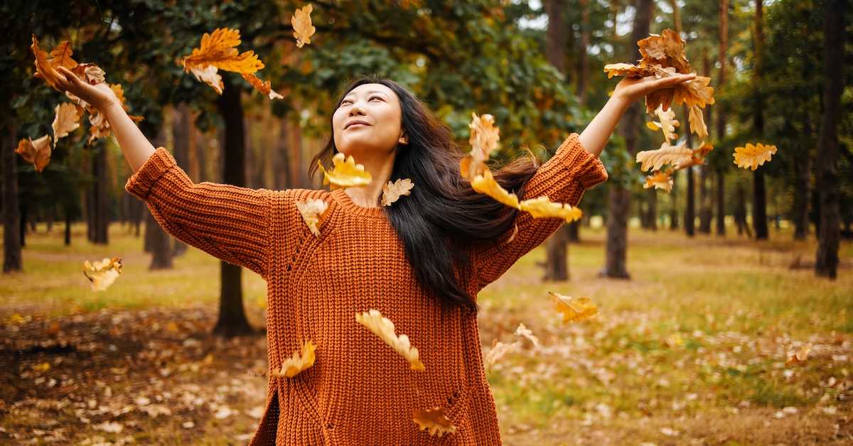 Casual joyful asian woman cheerfully throws leaves in autumn in city park